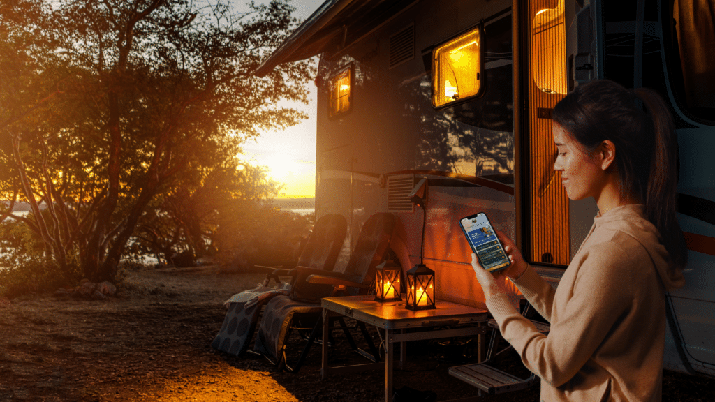 Guest viewing a No-Download Guest Hub on a smartphone beside an RV campsite at sunset.