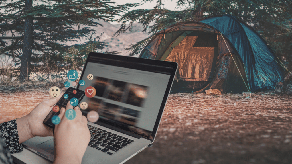 Person using a laptop and smartphone near a tent, creating social content for campground bookings and engagement.