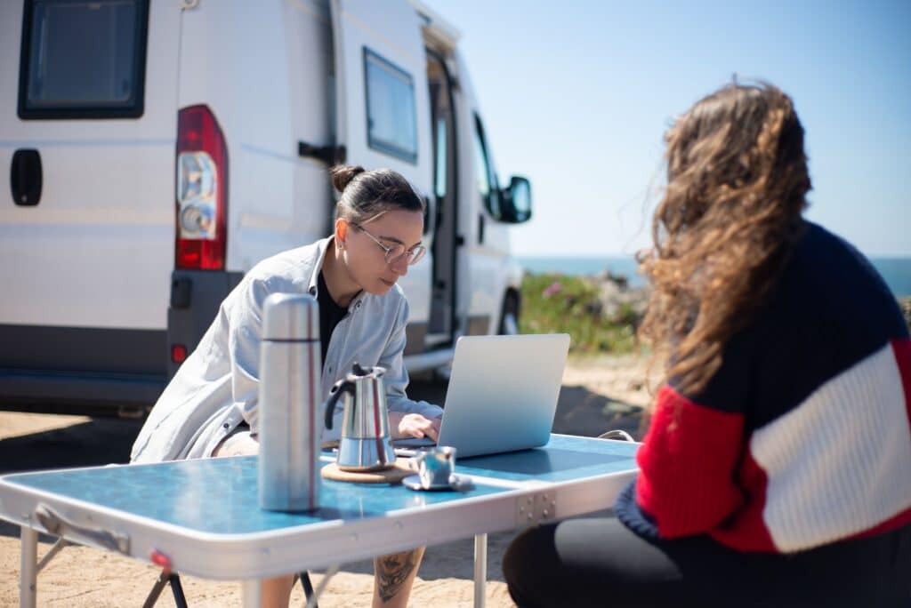 RV campers working on a laptop at an outdoor campsite beside their camper van.